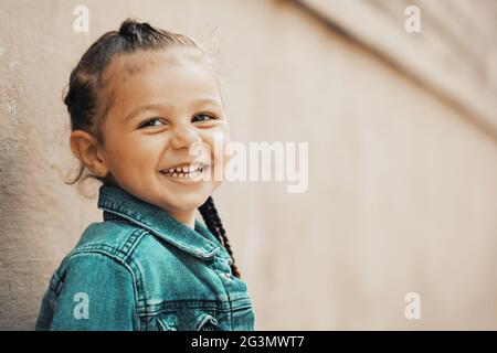 Mädchen in Jeansjacke lächelt an der Wand stehend. Hochwertige Fotos Stockfoto