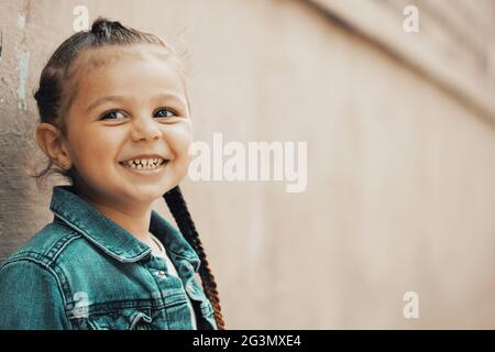 Mädchen in Jeansjacke lächelt an der Wand stehend. Hochwertige Fotos Stockfoto