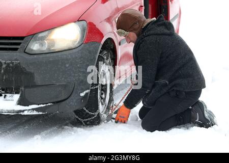 '12.02.2021, Graditz, Sachsen, Deutschland - Mann, der im Winter eine Schneekette auf einen Vorderreifen seines Autos legt. 00S210212D791CAROEX.JPG [MODELLVERSION: JA, PR Stockfoto