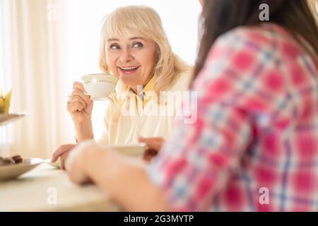 Lächelnde Frau trinkt Tee und unterhält sich gerne mit einer Tochter Stockfoto