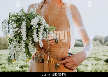 Junge Mädchen Floristin in Schürze schafft einen Blumenstrauß als Geschenk aus blühenden Wildblumen. Floristin bei der Arbeit.Frau hält Blumenstrauß Stockfoto