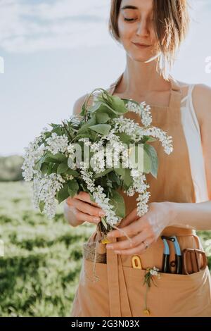 Junge Mädchen Floristin in Schürze schafft einen Blumenstrauß als Geschenk aus blühenden Wildblumen. Blumenhändler bei der Arbeit. Frau hält Blumenstrauß Stockfoto