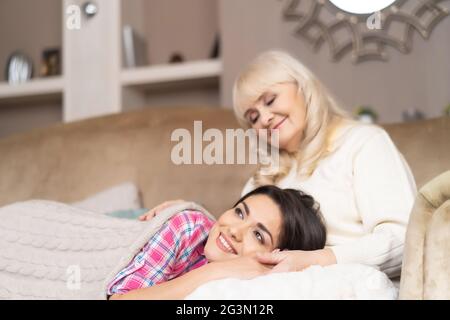 Charmantes Mädchen liegt auf den Knien der Mutter auf dem Sofa Stockfoto