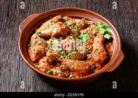 Chakhokhbili, geschmortes Huhn, Tomate mit frischen Kräutern, Walnüssen und Gewürzen in einem Tontopf auf einem Holztisch, georgische Küche Stockfoto