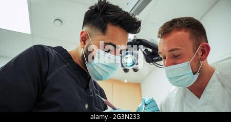 Zwei männliche Zahnärzte, die chirurgische Masken tragen und den Patienten operieren Stockfoto