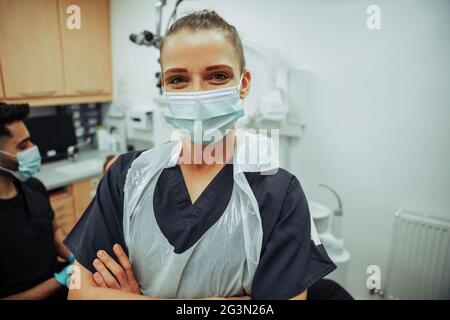 Kaukasische Krankenschwester, die lächelt und eine OP-Maske trägt, während sie mit einem männlichen Kollegen im Zimmer des Arztes steht Stockfoto