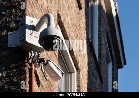 Zwei verschiedene Arten von Überwachungs- oder Überwachungskameras an einer Ziegelwand eines Ladens im Zentrum von Maastricht, Niederlande. Blauer Himmel Stockfoto