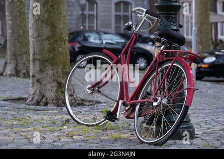 Rotes Fahrrad mit einem flachen Hinterreifen ist auf einem Platz in Maastricht gegen einen antiken Laternenpfosten gesperrt Stockfoto