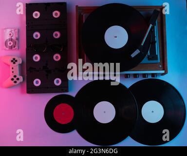 Retro-Medien- und Unterhaltungsartikel der 80er Jahre. Vinyl-Player, Video, Audiokassetten, 3D-Brille, Gamepad. Neonlicht. Draufsicht Stockfoto