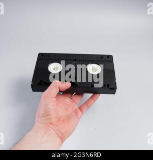 Männliche Hand hält die Retro-Videokassette auf grauem Hintergrund. Stockfoto