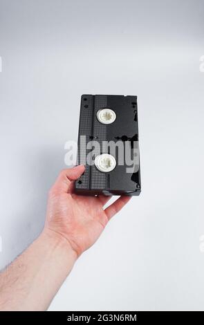 Männliche Hand hält die Retro-Videokassette auf grauem Hintergrund. Stockfoto