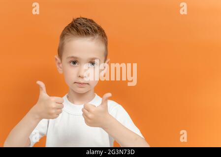 Foto von positiven Vorschuljunge zeigen Daumen bis Zeichen tragen mit zwei Händen isoliert über orange Hintergrund. Kinderstudio Porträt. Stockfoto