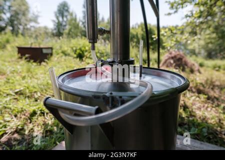 Alkoholmashine in einem Dorfhof, auf einem verschwommenen Hintergrund. Zubereitung eines berauschenden Getränks. Nahaufnahme. Stockfoto