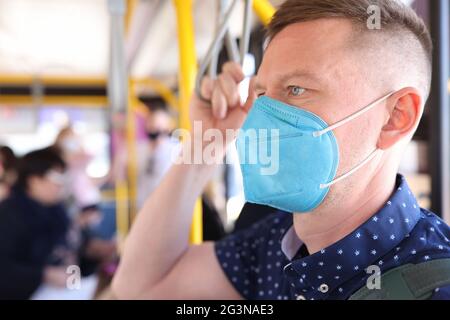 Mann trägt eine schützende medizinische Maske, fährt mit dem Bus und hält sich am Handlauf fest Stockfoto
