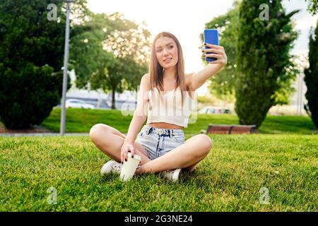 Glücklich lächelnde blonde Frau macht Selfie per Handy, Outdoor.Konzept der Urlaub Lebensstil. Schönes Mädchen mit Smartphone im Park.Sonniger Tag. Glückskonzept. Hochwertige Fotos Stockfoto