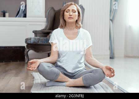 Eine Frau im Alter von über 50 Jahren ist Yoga zu Hause. Stockfoto