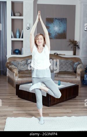 Eine 50 Jahre alte Frau übt Yoga zu Hause im Wohnzimmer. Stockfoto