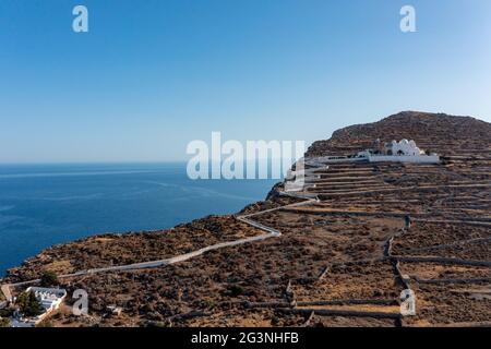 Insel Folegandros, Griechenland, Kykladen. Panagia Jungfrau Maria Kirche und lange Zickzack Straße Luftdrohne Ansicht. Traditionelle kykladische, weiß getünchte Kirche an Stockfoto