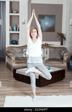 Eine 50 Jahre alte Frau übt Yoga zu Hause im Wohnzimmer. Stockfoto