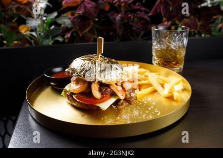 Lachs- und Shrimp-Burger, Mayonnaise auf dem Bottom Bun, paniertes Lachs-Shrimp-Patty und Tartarsauce mit frischen Garnelen auf grauem Holzbrett Hintergrund Stockfoto