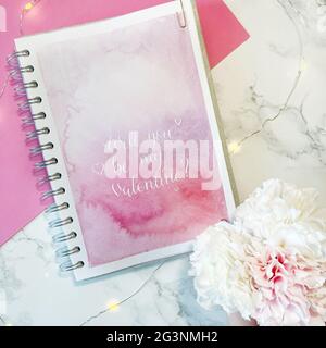 Wirst du mein Valentinstag sein? - weiße Tinte Kalligraphie Kupferplatte Stil auf rosa Aquarell Hintergrund in Skizzenbuch Stockfoto