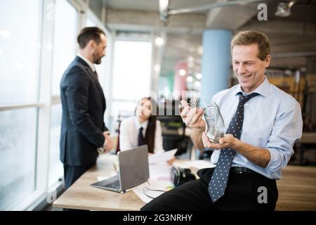 Ein Geschäftsmann spielt mit einem Metallspielzeug, das slinky ist. Büroangestellte sprechen im Büro dahinter Stockfoto