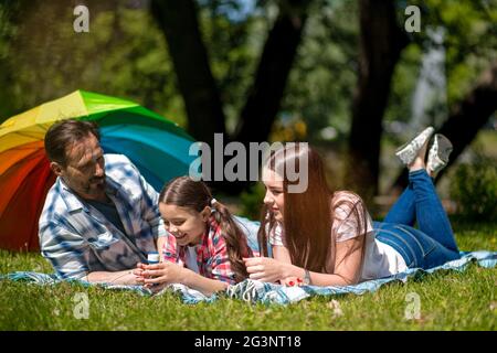 Familie liegen zusammen auf einer Picknickdecke draußen im Park. Bunten Regenschirm auf dem Hintergrund. Stockfoto