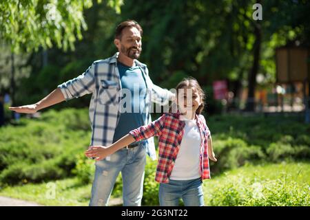 Vater Zeit mit Tochter in den Park während Standind Whith Wild geöffnet Hände und lächelt. Stockfoto