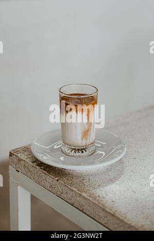 Schmutziger Kaffee in einem Glas auf einem weißen Tisch mit Sonnenlicht in der früh platziert. Stockfoto