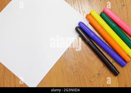 Eine Reihe von farbigen Markierungen und ein weißes Blatt Papier auf dem Tisch. Stockfoto