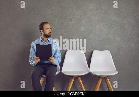 Junger Mann, der auf einem Stuhl sitzt, den Lebenslauf hält und auf ein Vorstellungsgespräch wartet Stockfoto