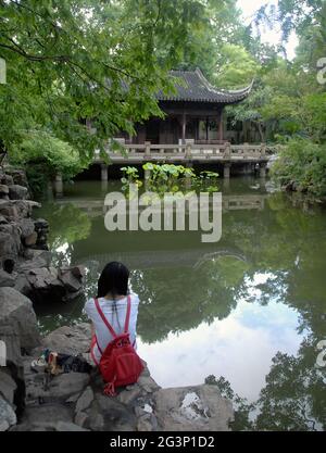 Yu Yuan Garten in der Altstadt von Shanghai, EIN traditioneller chinesischer Garten mit Bäumen, Felsen und Wasser. Eine Frau mit Blick auf einen See und einen Pavillon. Stockfoto