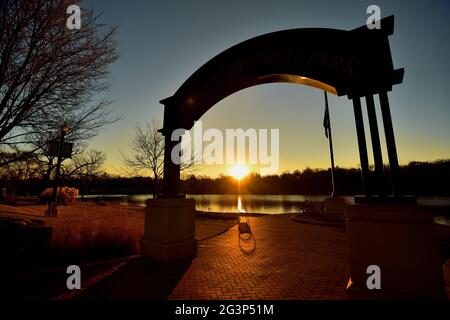 Elgin, Illinois, USA. Der Sonnenuntergang spiegelt sich am Fox River wider, der durch den Bogen im Veterans Memorial Park in Elgin, Illinois, gesehen wird. Stockfoto