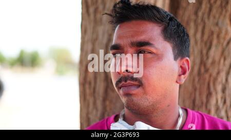 Seitenansicht des indischen Mannes mit Maske und Hemd über Baumstamm Hintergrund mit ernstem Gesicht. Stockfoto