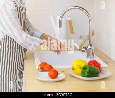 Gesichtslose ältere Frau in der Schürze, die Gemüse für Salat zubereitet, während sie in der modernen Küche zu Hause kocht Stockfoto