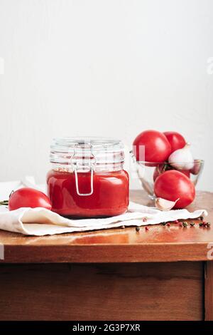 Tomatenmark in einem Glas. Sauce, frische Tomaten, Knoblauch und Paprika auf einem hölzernen Küchentisch. Stockfoto