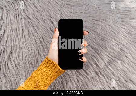 Gepflegte Womans Hand hält Smartphone auf grau flauschigen Hintergrund Stockfoto