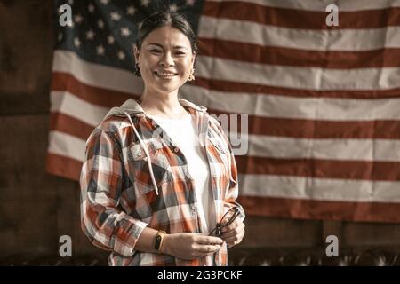 Lächelnde asiatische Frau posiert stolz auf der gestreiften amerikanischen Flagge zurück Stockfoto