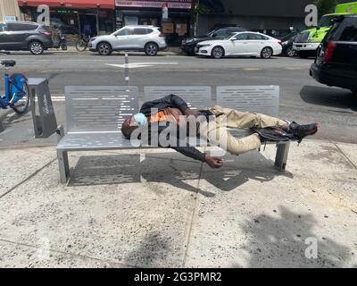 Obdachloser schläft auf einer Bank entlang der Church Avenue im Stadtteil Kensington in Brooklyn, New York, mit einer Gesichtsmaske während der Covid-19-Pandemie. Stockfoto