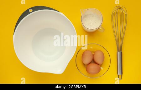 Schneebesen und eine Plastikbecher zum Schlagsacken auf gelbem Hintergrund. Stockfoto