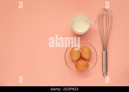 Schneebesen und eine Plastikbecher zum Schlagsacken auf einem rosa Hintergrund. Stockfoto