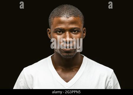 Ernsthafter afroamerikanischer Mann, der die Kamera anschaut, attraktiver junger Mann mit dunkelhäutiger Haut in einem weißen T-Shirt, in dem er Confi ausdrückt Stockfoto