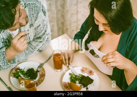 Body positive Paar isst gesunde Lebensmittel während der Sitzung am Küchentisch, Männer und Frauen essen Salat und Obst auf ihren Tellern geschnitten Stockfoto