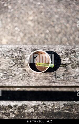 Geschmolzenes Eis in einer Tasse mit einem Löffel auf einer Bank. Heißer Sommertag. Stockfoto