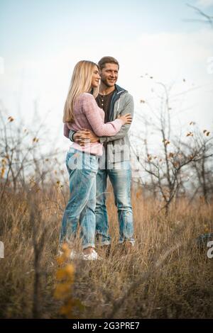 Umarmend paar lächelnd stehend auf Herbstgras im Freien, junge Jungs kuscheln in der Natur gegen einen blauen Himmel Stockfoto