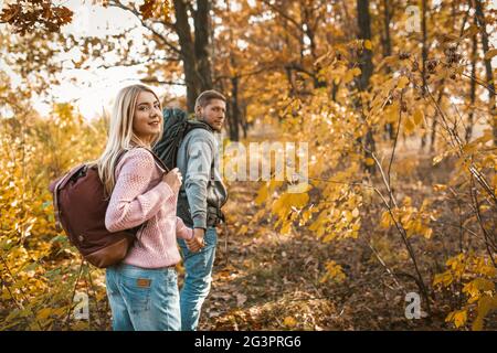 Lächelndes paar Touristen, die auf einem Waldweg entlang gehen und die Hände halten und auf die Kamera zurückschauen Stockfoto