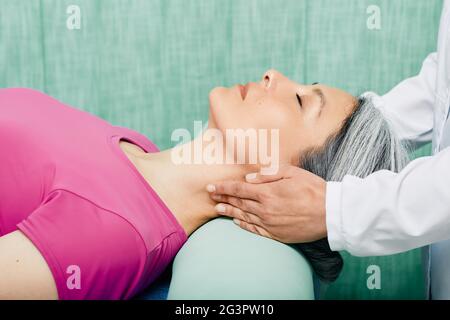 Die Patientin, die auf einem Massageliegen liegt, erhält vom osteopathischen Arzt eine therapeutische Massage des Halses und der oberen Wirbelsäule Stockfoto