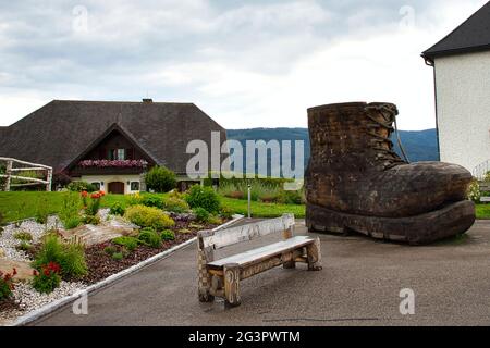 ÖSTERREICH, STEIERMARK, SOBOTH - 25. JULI 2020: Auf dem Dorfplatz von Soboth befindet sich eine Skulptur eines riesigen Wanderschuhs neben einer Banch Stockfoto