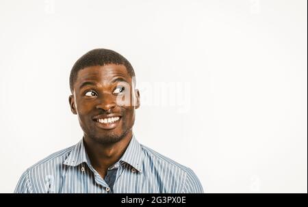 Lächelnder afroamerikanischer Mann schaut spielerisch zur Seite. Junger Geschäftsmann mit Kopierfläche auf der rechten Seite. Gesunde Zähne konz Stockfoto