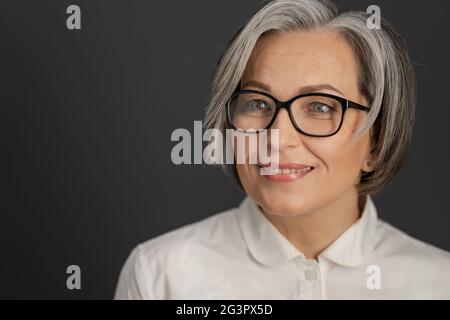 Hübsche grauhaarige Frau in weißem Hemd. Intelligente Geschäftsfrau mittleren Alters in einer Brille mit mittellangen Pflege Frisur smil Stockfoto